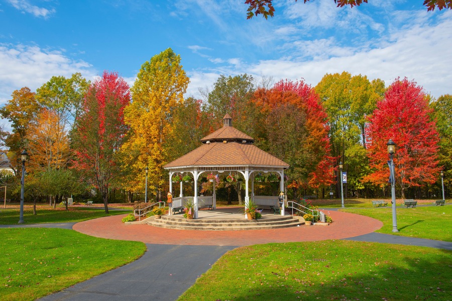 A gazebo in a park surrounded by autumn-colored trees.