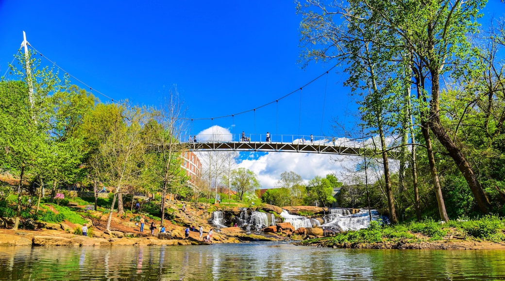 A bridge over a river with a waterfall, surrounded by trees and greenery.