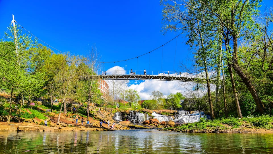 A bridge over a river with a waterfall, surrounded by trees and greenery.