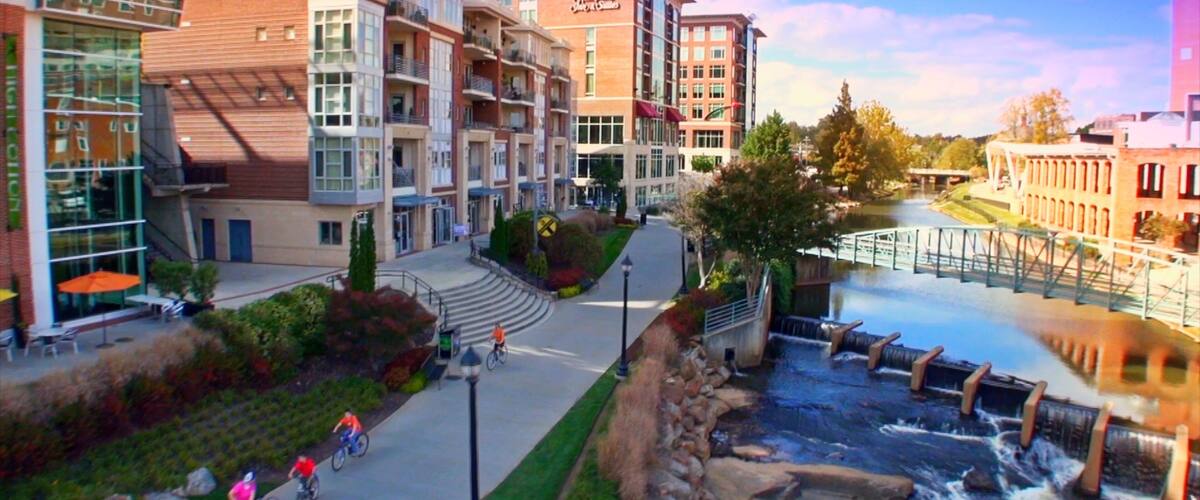 A riverside walkway with cyclists, a bridge, and modern buildings.