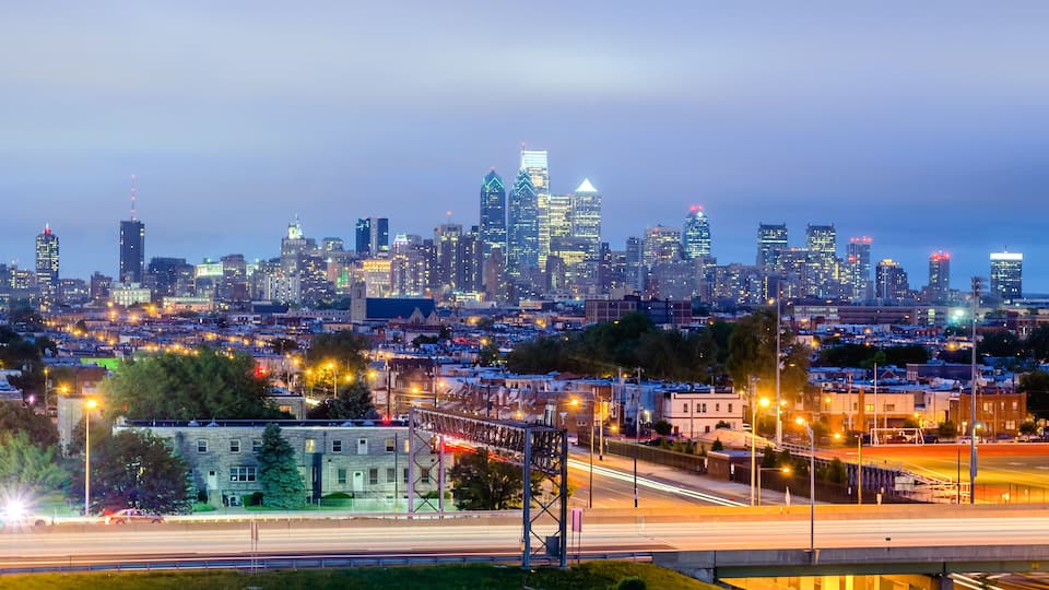 A city skyline at dusk with illuminated buildings and a highway in the foreground.