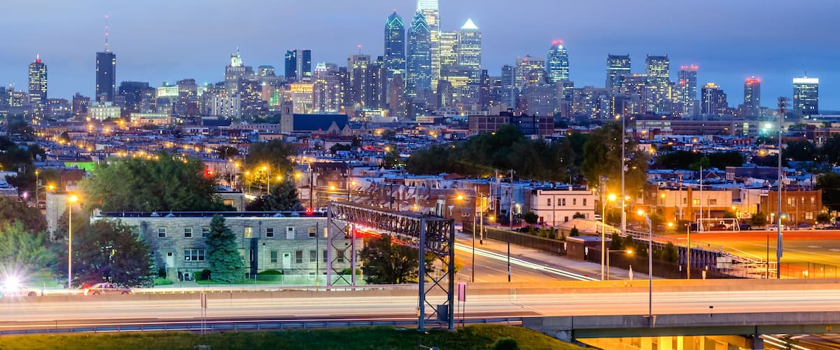 A city skyline at dusk with illuminated buildings and a highway in the foreground.