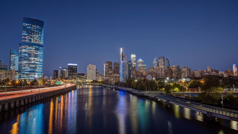 A nighttime city skyline with illuminated buildings and a river reflecting lights.