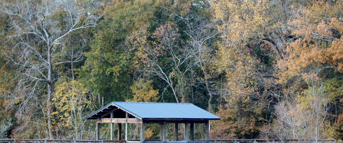 A wooden pier extending over a calm lake, with a covered shelter at the end.