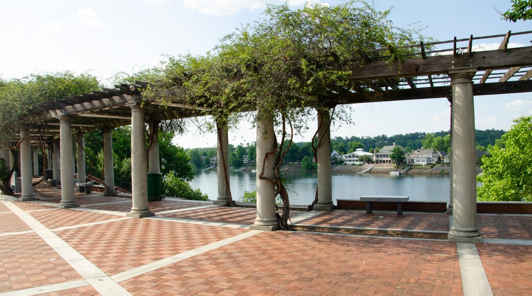 A section of a river walk with a shaded rest area under a pergola, with white columns. There is a view of the river.