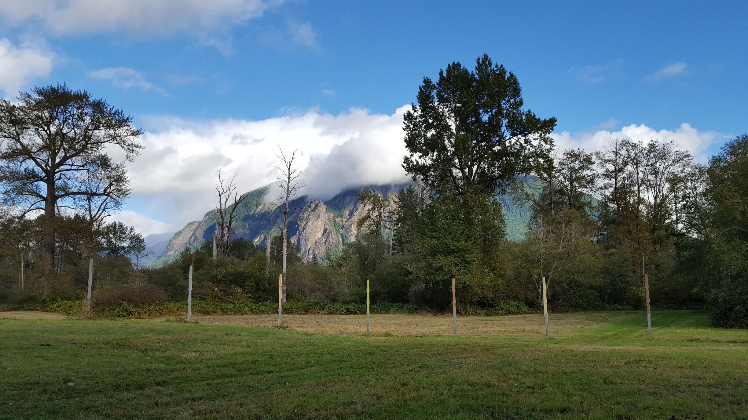 The plaque reads: "This installation is part of a planned set of artworks honoring Snoqualmie elder Xa-cha-blu, usually known as Marie Louie [...] The cedar markers in the meadow indicate the position of the rising sun at various times of the year, their colors key to their traditional name."