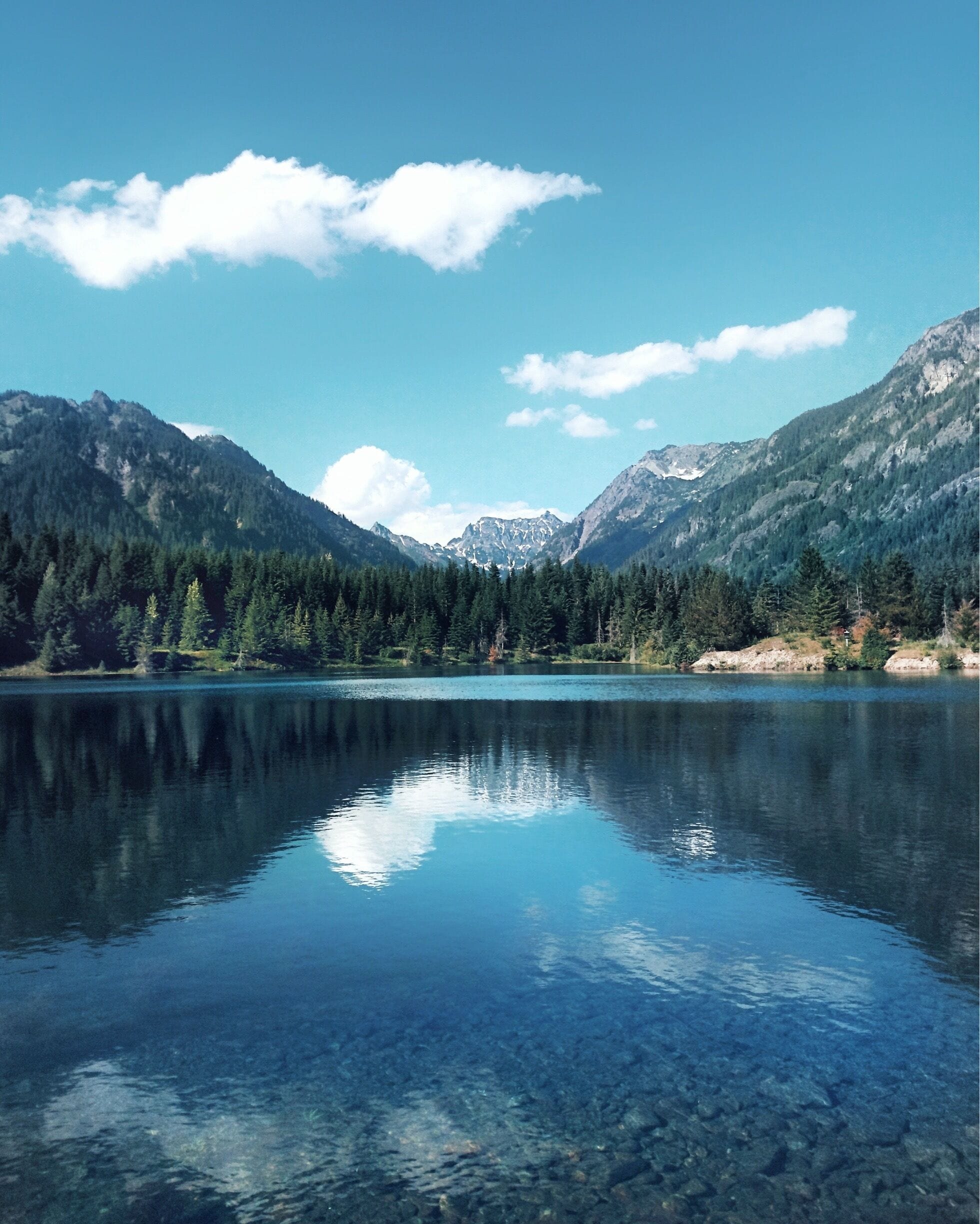 A clear lake surrounded by mountains and dense forests.