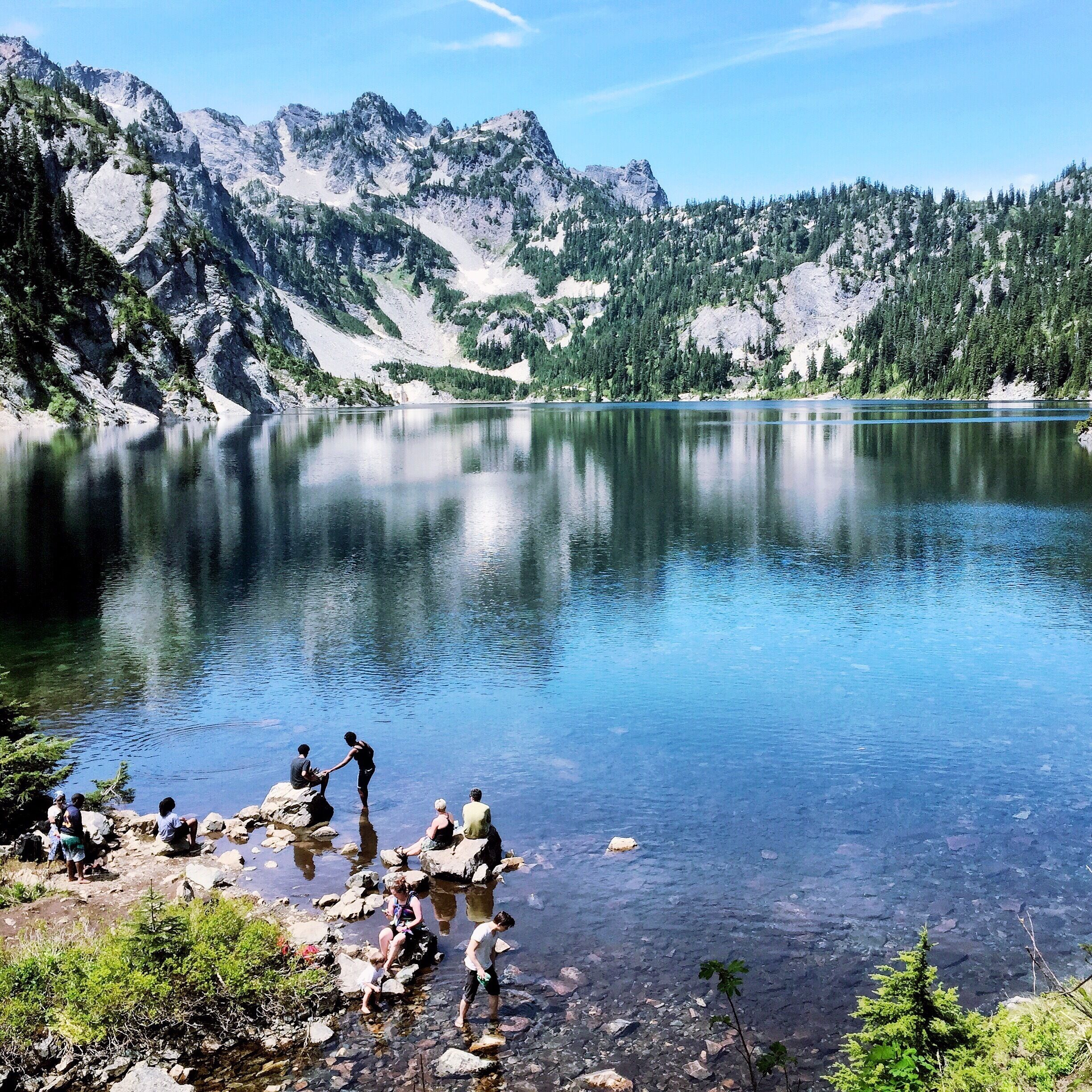 A clear mountain lake surrounded by rocky terrain and dense forests.