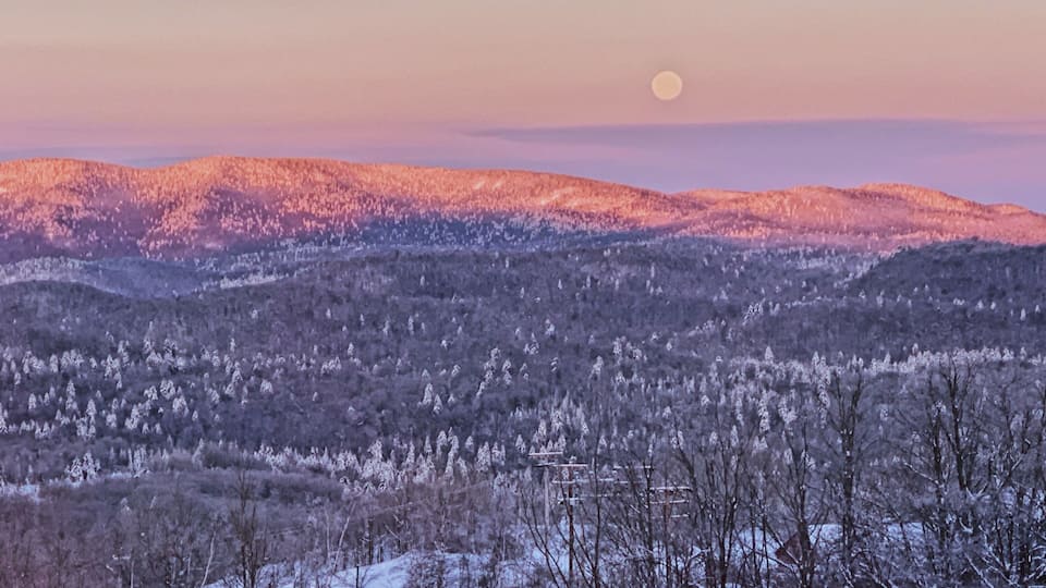 A snow-covered landscape with a mountain range and a full moon in the sky.