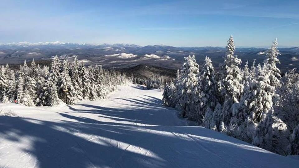 A snow-covered mountain path with trees and distant snow-capped peaks under a clear sky.