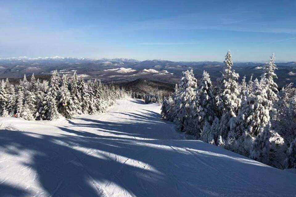 A snow-covered mountain path with trees and distant snow-capped peaks under a clear sky.