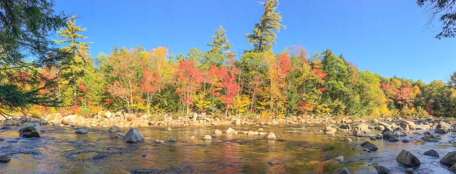 A river with clear water, surrounded by rocks and trees with autumn foliage.