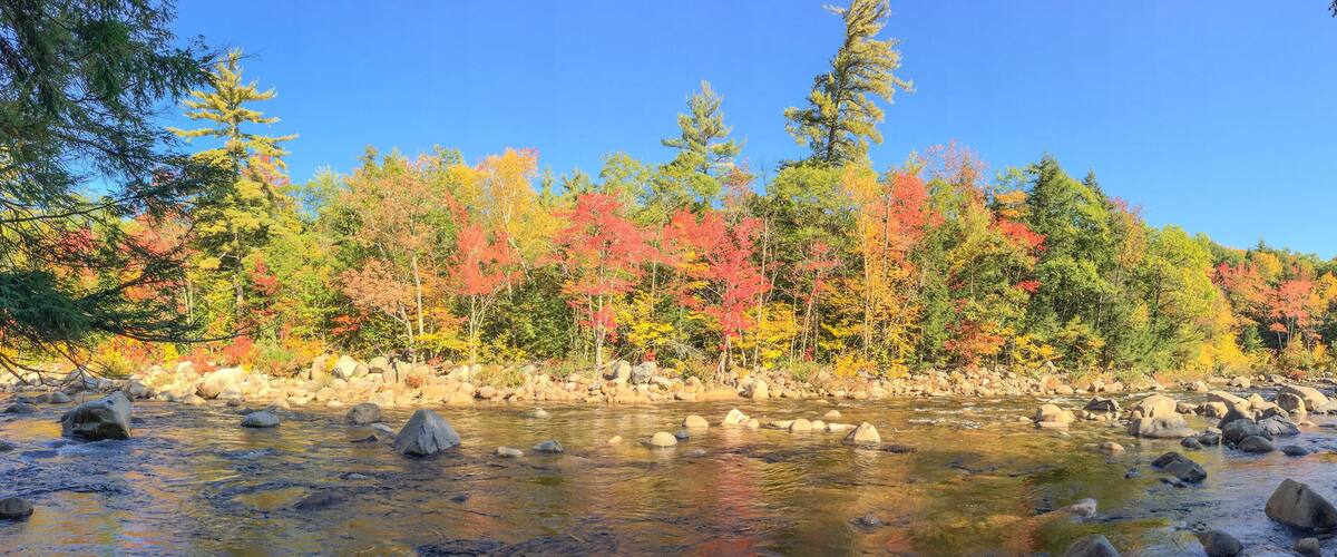 A river with clear water, surrounded by rocks and trees with autumn foliage.