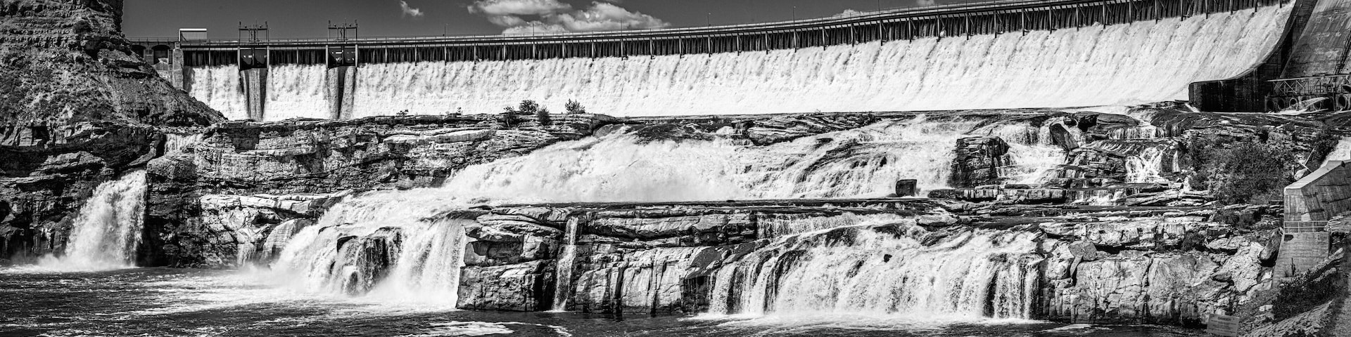 A large dam with multiple spillways releasing water into a river.