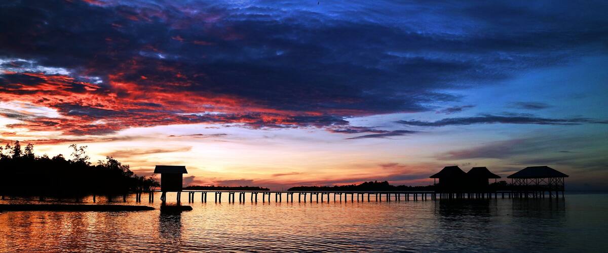 A sunset over a calm lake with overwater bungalows and a pier.
