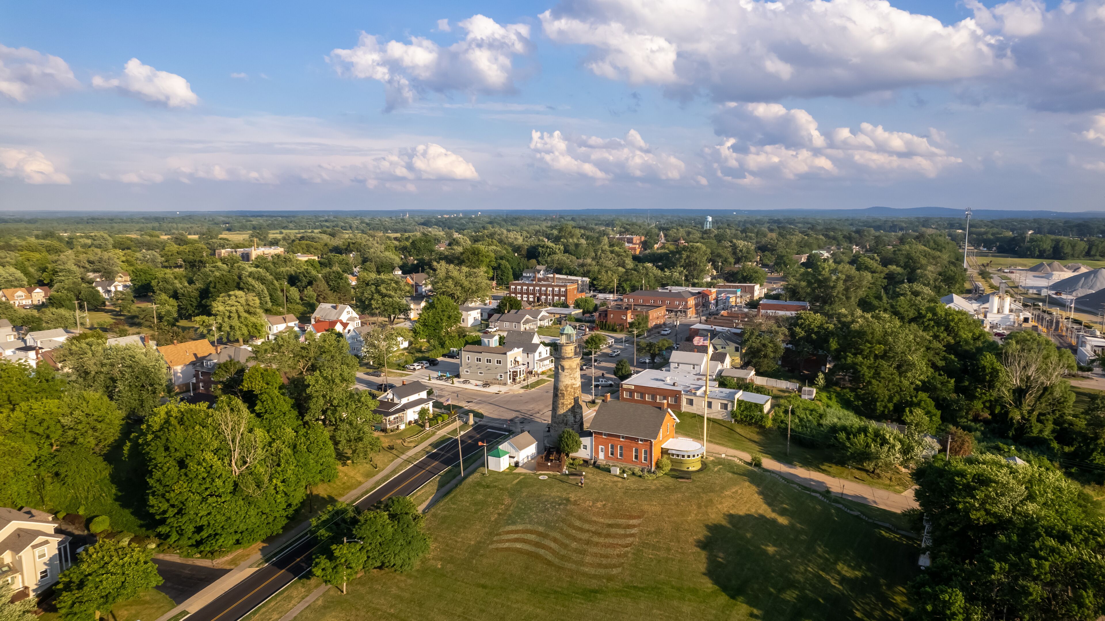 An aerial view of a town with a prominent tower, a mix of residential and commercial buildings, and surrounding greenery.
