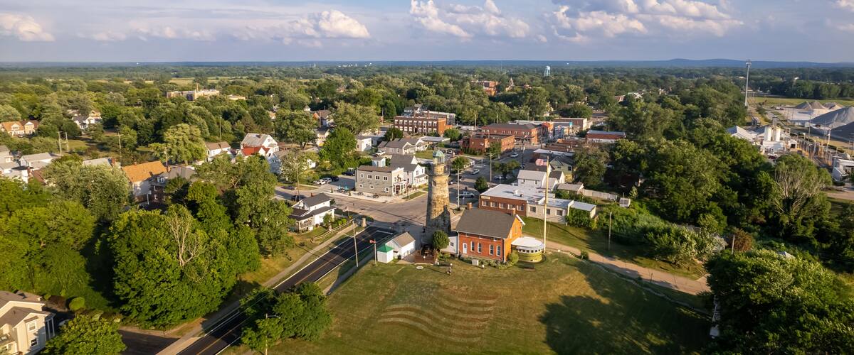 An aerial view of a town with a prominent tower, a mix of residential and commercial buildings, and surrounding greenery.