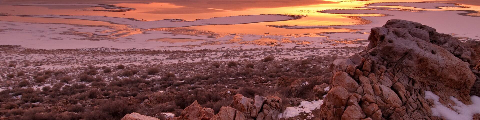A rocky landscape with a sunset over a body of water.