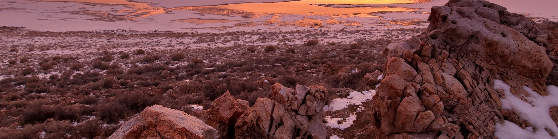 Un paisaje rocoso con el atardecer sobre un cuerpo de agua.
