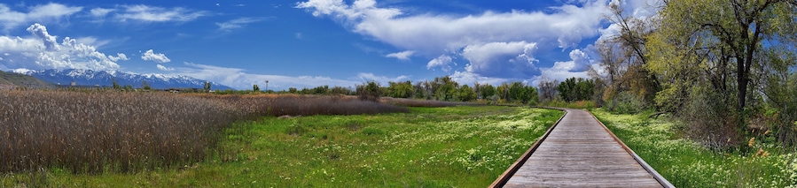 Jordan River Parkway Trail, Redwood Trailhead bordering the Legacy Parkway Trail, panorama views with surrounding trees and silt filled muddy water along the Rocky Mountains, Salt Lake City, Utah.