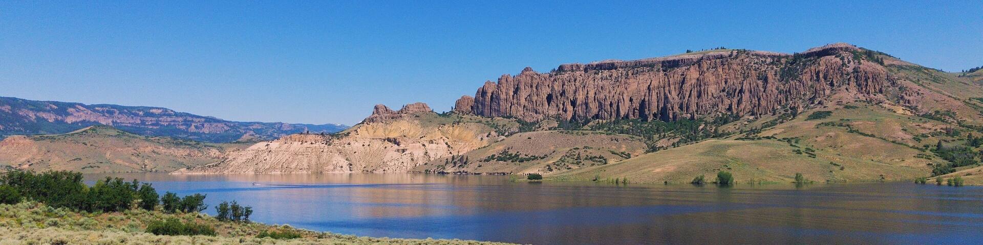 A lake surrounded by grassy hills and a rocky cliff.