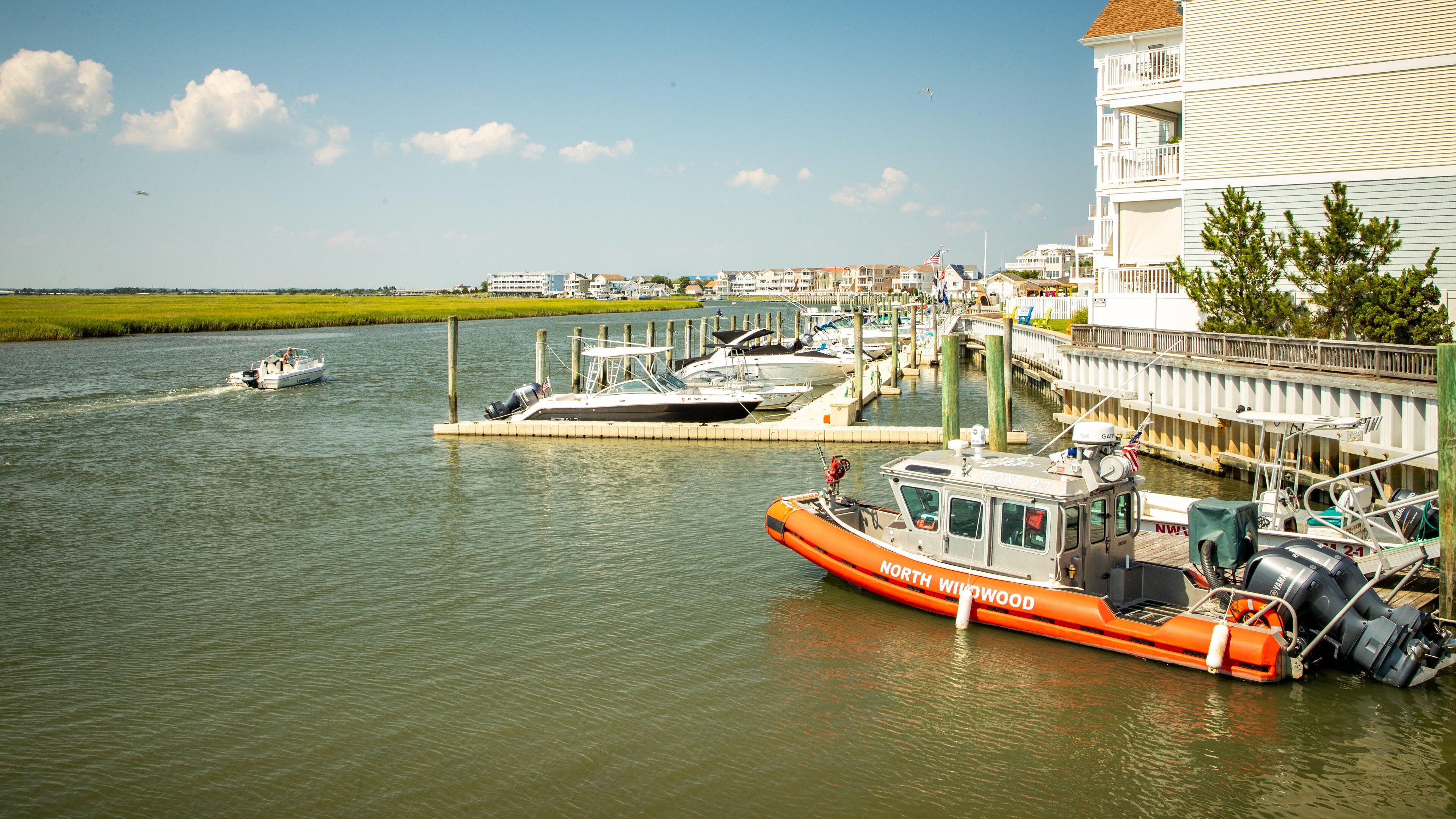 A marina with boats docked, a bridge, and a white building with a balcony.