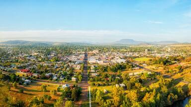 Uma cidade com uma rua central, vegetação ao redor e montanhas ao longe.