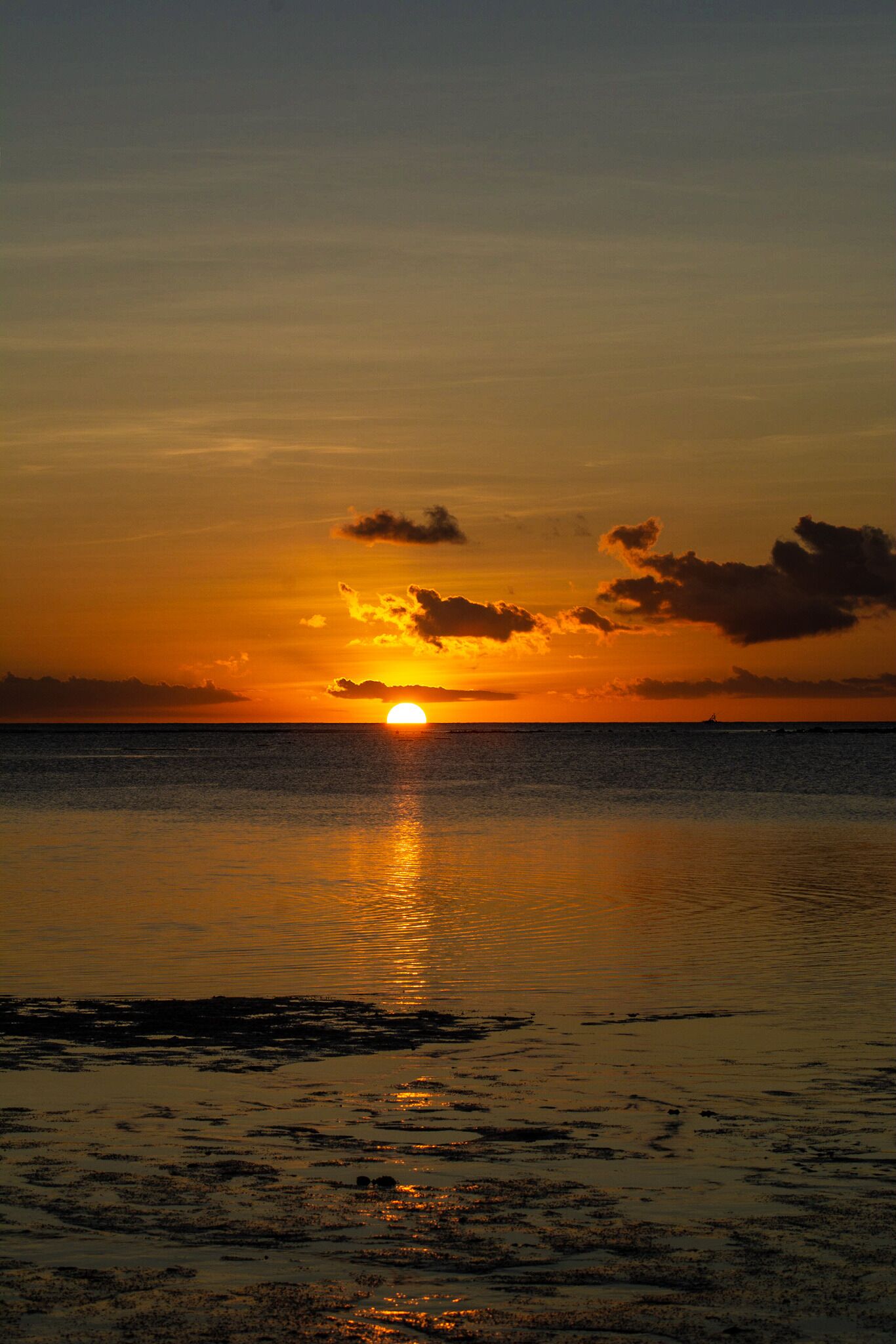 A sunset over a calm sea with a visible boat on the horizon.