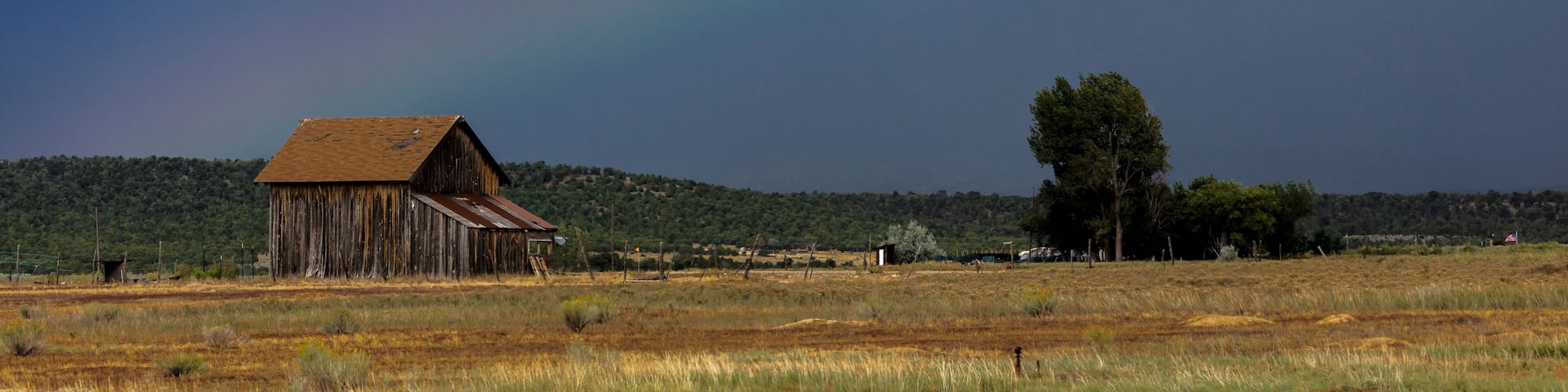 Dramatic view of rainbow over a western barn near Norwood Colorado in the LaSalle Mountains