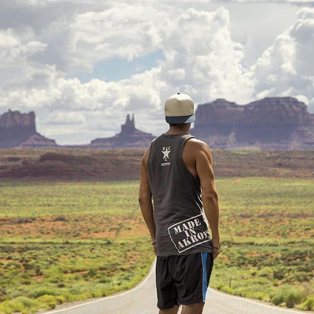 A person standing on a road with a desert landscape and mountains in the background.