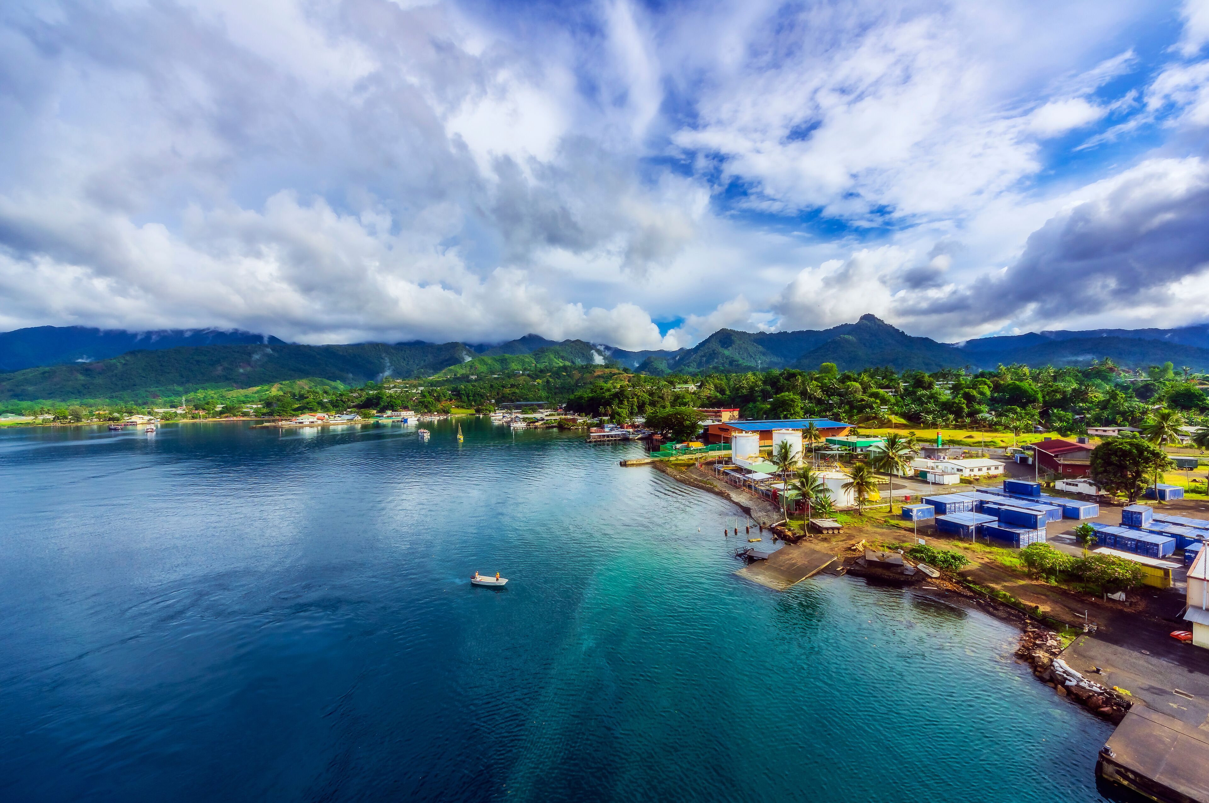 A coastal town with a clear view of the ocean, mountains in the background, and a small boat on the water.