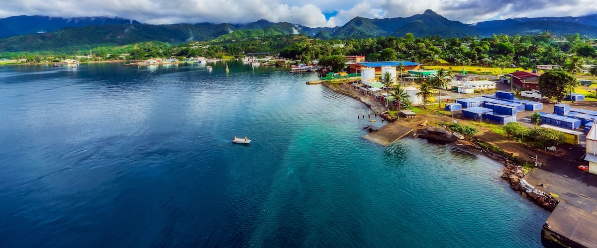 A coastal town with a clear view of the ocean, mountains in the background, and a small boat on the water.