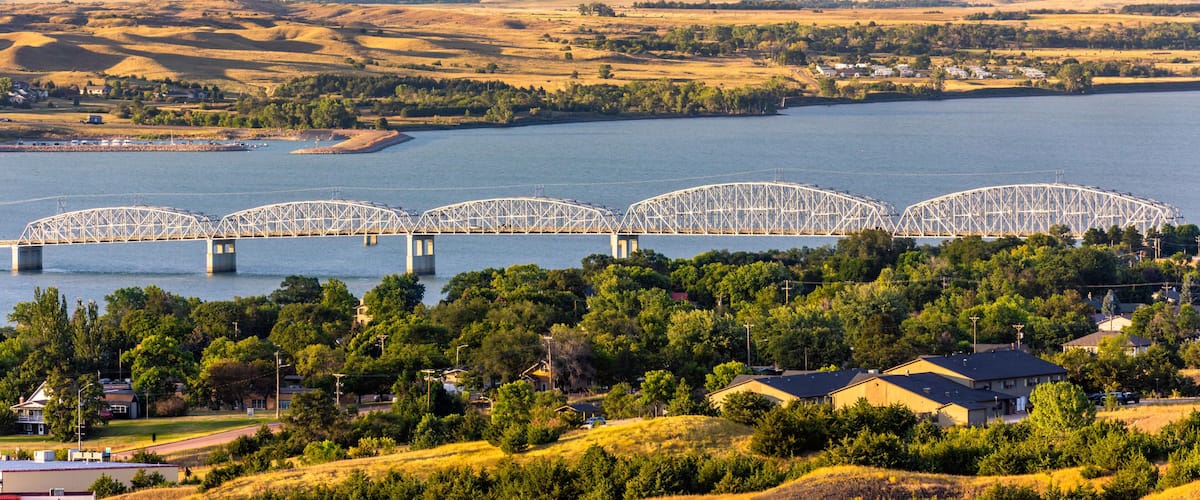A large river with a bridge spanning across it, surrounded by hills and a small town with houses.