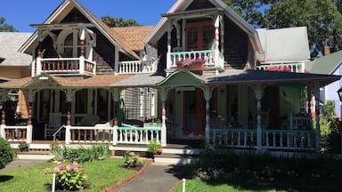 Una casa histórica de dos pisos con un balcón y un porche, rodeada de un jardín bien cuidado.