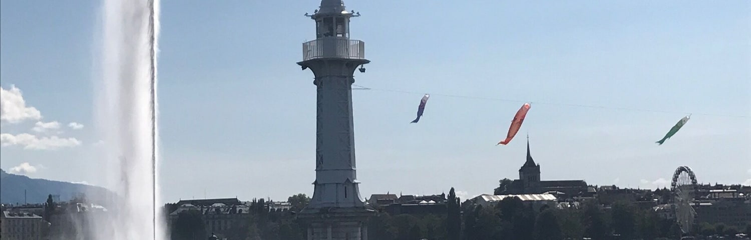 Un faro junto al agua, con una fuente y cometas al fondo.