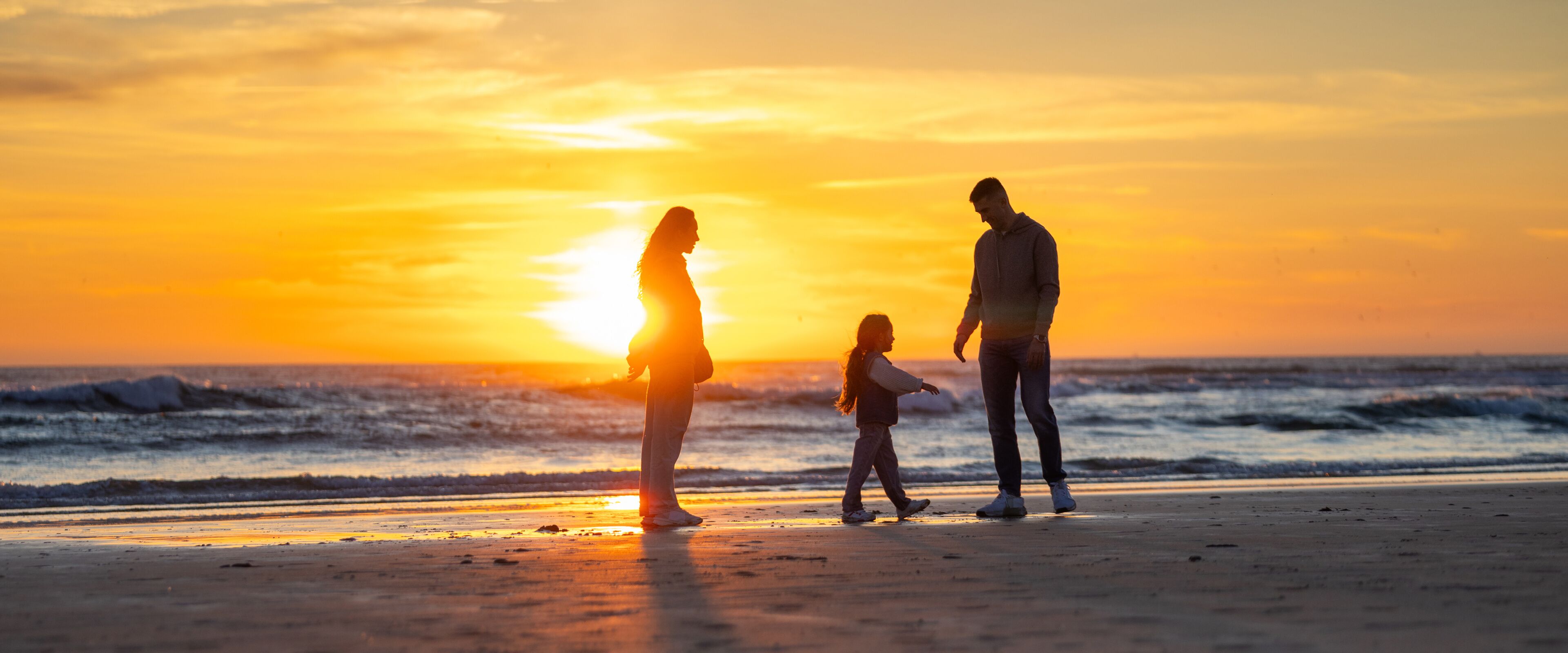 Family walking together on ocean beach at sunset