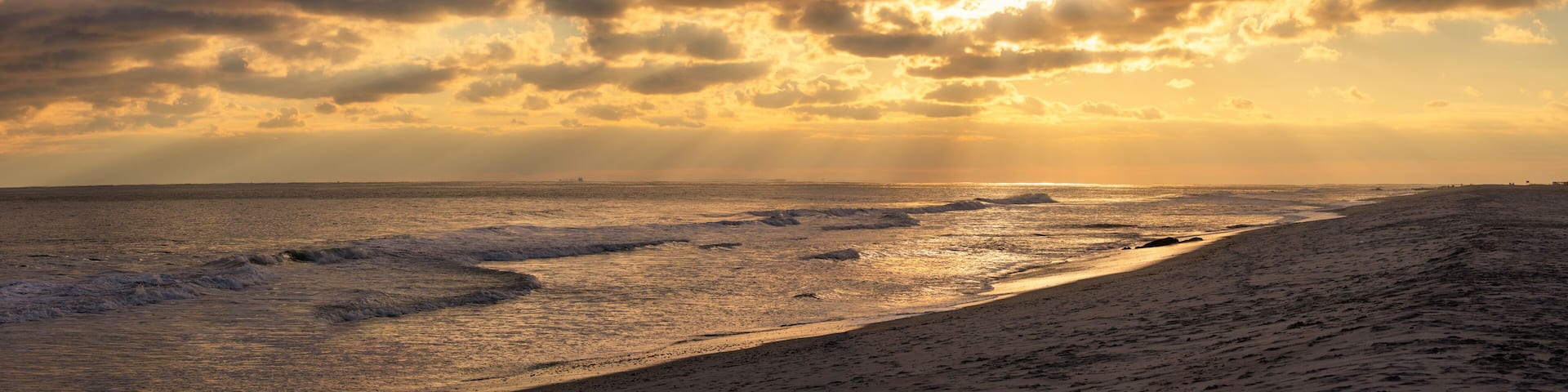 Beams of sun poking through clouds over a beach during sunset. Long Island New York panorama