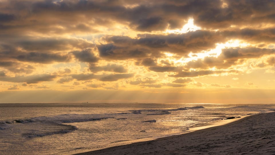 A beach with waves and a cloudy sky.