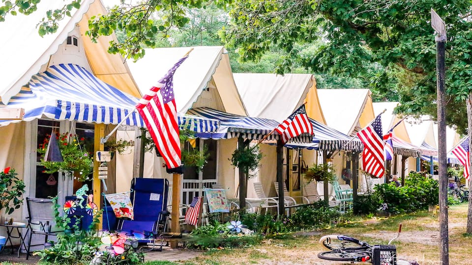 A row of tents with American flags, surrounded by greenery and a bicycle.
