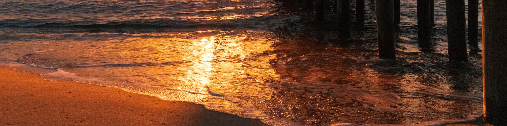 A pier extending into the ocean at sunset with a clear sky.