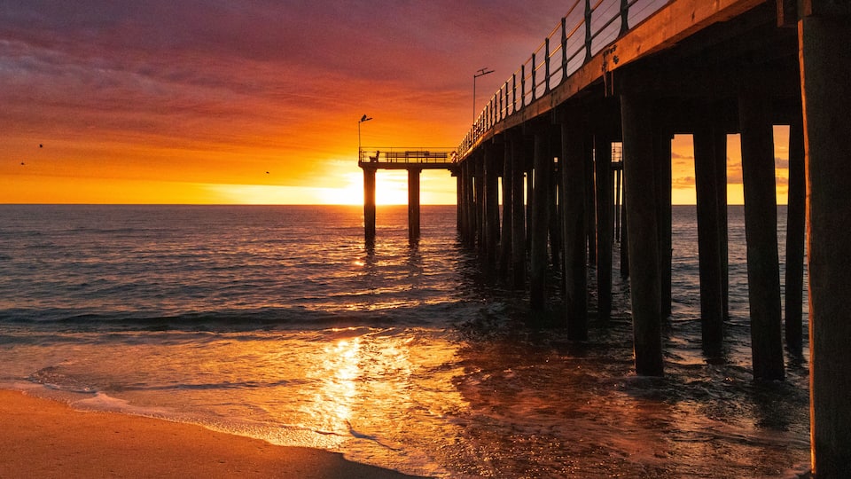A pier extending into the ocean at sunset with a clear sky.