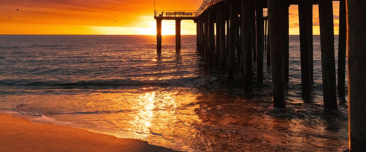 A pier extending into the ocean at sunset with a clear sky.