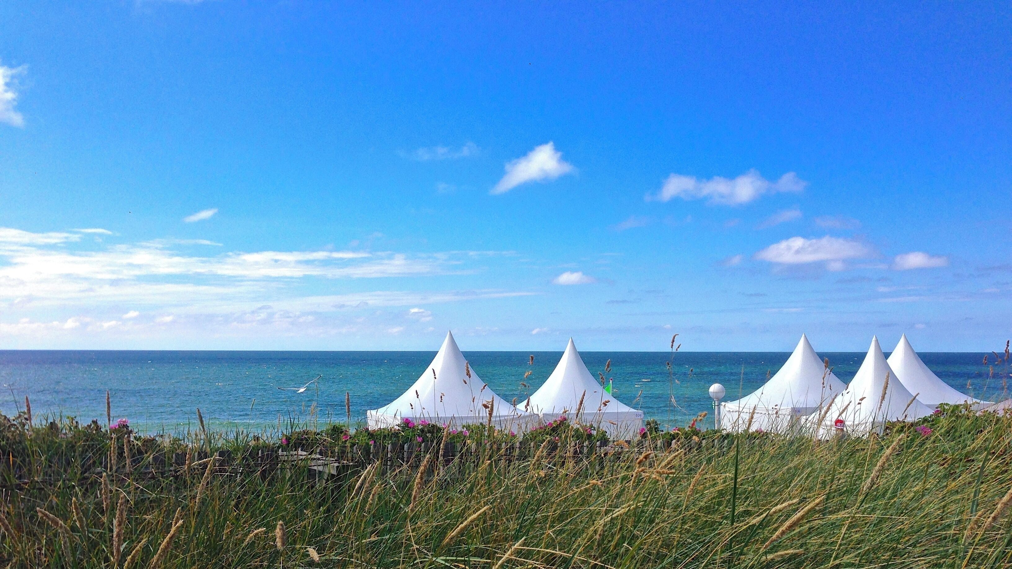 A beach with white tents and the ocean in the background.