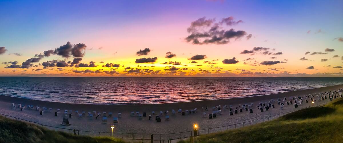 A beach at sunset with rows of beach chairs and umbrellas, and the ocean in the background.