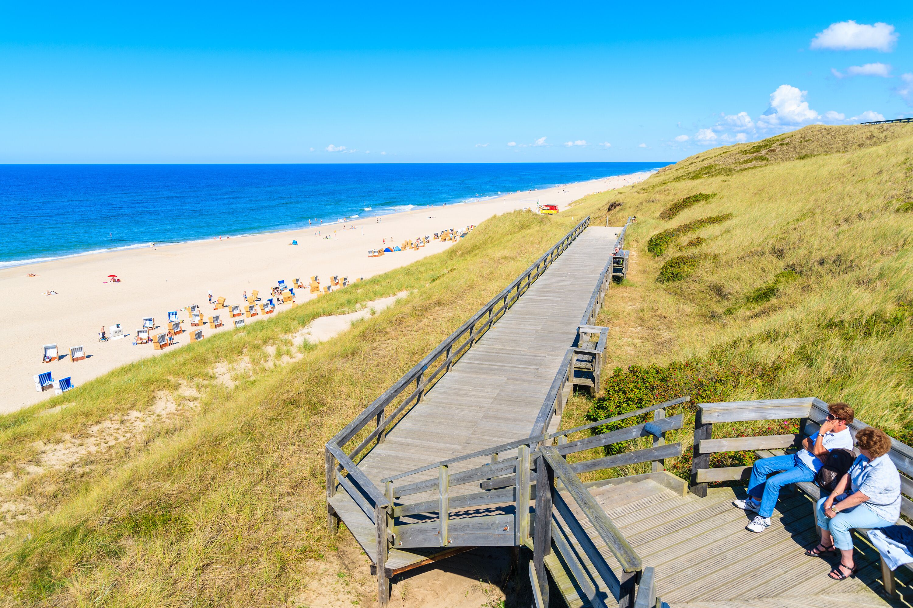People sitting on coastal promenade along beach in Wenningstedt town, Sylt island, Germany