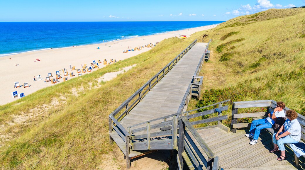People sitting on coastal promenade along beach in Wenningstedt town, Sylt island, Germany