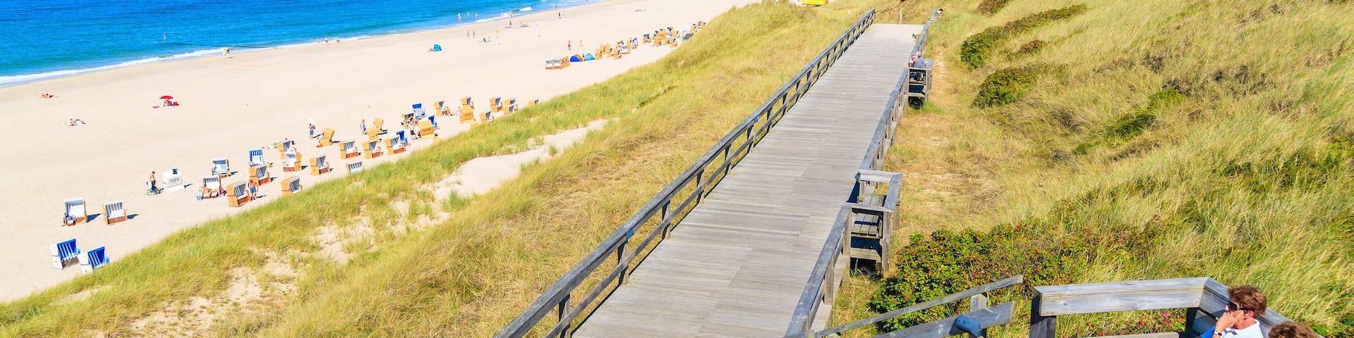 People sitting on coastal promenade along beach in Wenningstedt town, Sylt island, Germany