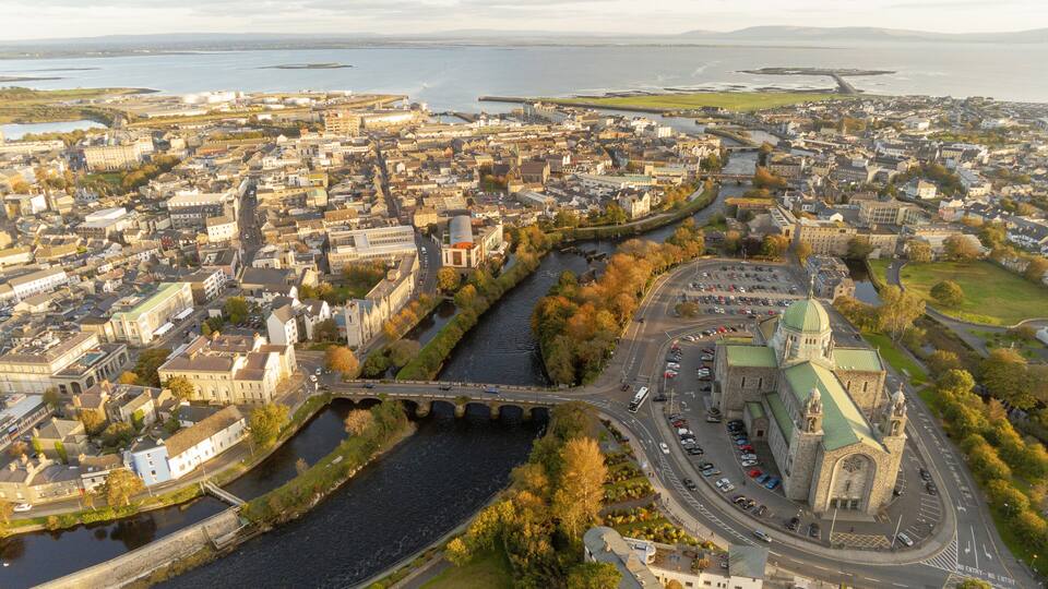 A river flowing through a city with historic buildings and a prominent church with a green roof.