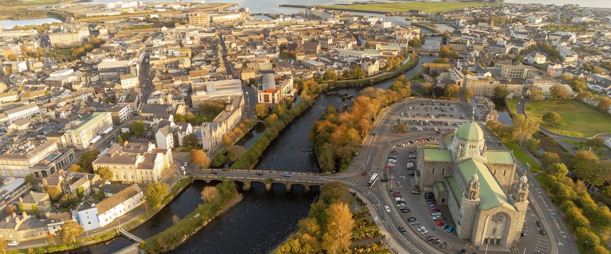 A river flowing through a city with historic buildings and a prominent church with a green roof.