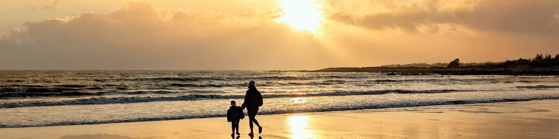 Une plage au coucher du soleil, avec des vagues et deux personnes qui se promènent.